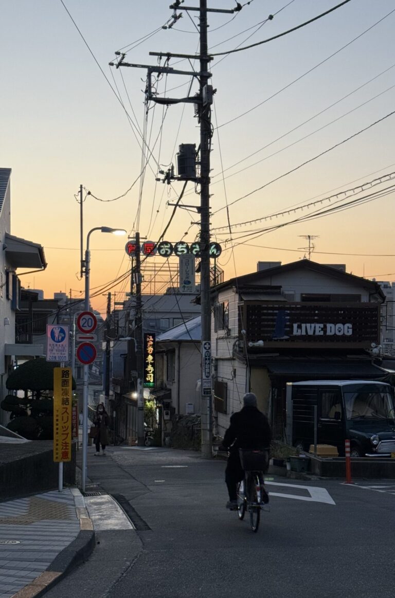 Couché de soleil sur Yanaka. Batiment avec Néon et vélo descendent la route.
